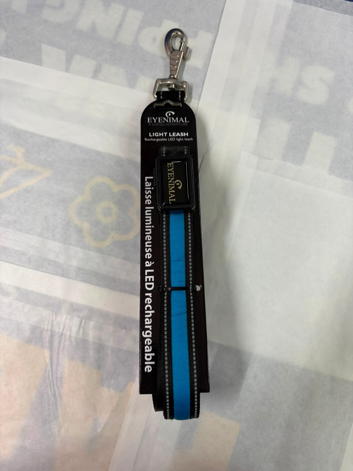 A black Eyensmal Light Leash LED dog leash with a blue center stripe and silver metal clasp, shown in its retail packaging on a patterned white surface.